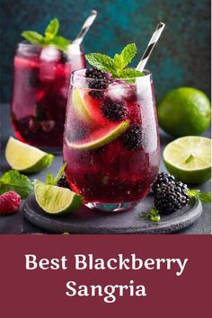 two glasses filled with blackberry sanggraa on top of a black slate plate next to limes and raspberries