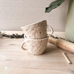 two coffee cups with hearts painted on them are next to a plant and pencils