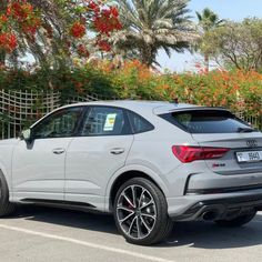 the rear end of an audi suv parked in a parking lot with trees and flowers behind it