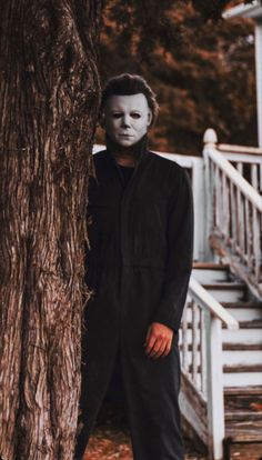 a man wearing a mask standing next to a tree