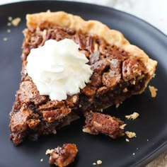 a piece of pecan pie with whipped cream on top is sitting on a black plate