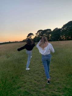 two women walking through a field at sunset