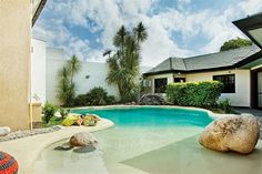 an outdoor swimming pool surrounded by rocks and palm trees with a house in the background