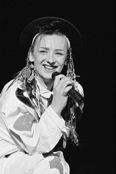 a woman wearing a hat and holding a microphone in her hand, smiling at the camera