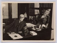 an old black and white photo of a man sitting at a desk in front of a bookcase