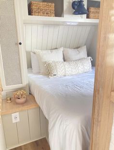 a bed with white linens and pillows in a small room next to a book shelf