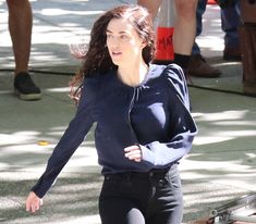 a woman is walking down the street in tight black pants and a blue top with long sleeves