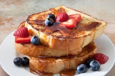 two pieces of french toast on a white plate with berries and syrup drizzled over them