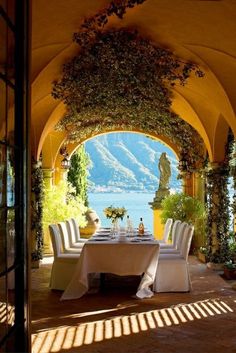 an outdoor dining area with tables, chairs and flowers on the arch over looking water