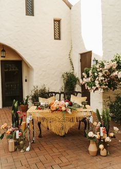 a table with flowers and candles on it in front of a white stucco building surrounded by potted plants