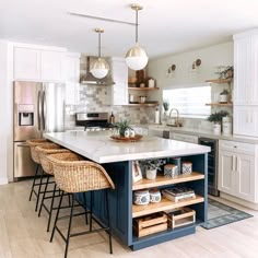 a kitchen with white cabinets and blue island in the center is surrounded by wicker bar stools