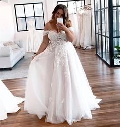 a woman in a white dress taking a selfie with her cell phone while standing on a wooden floor