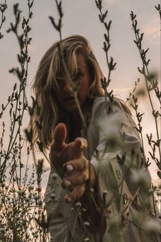 a woman standing in the middle of tall grass pointing her finger at something with both hands