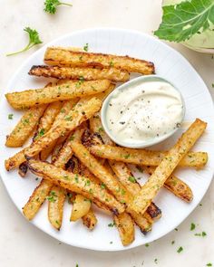 a white plate topped with french fries covered in ranch dressing next to a green leaf