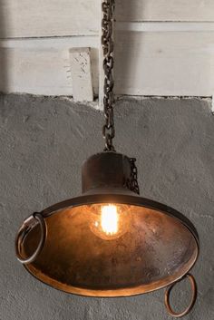 an old light hanging from a chain on the wall in a room with concrete walls