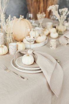 the table is set with white pumpkins and silverware