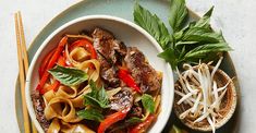 a bowl of noodles with meat and vegetables on a plate next to chopsticks