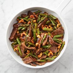 a white bowl filled with meat and asparagus on top of a marble counter