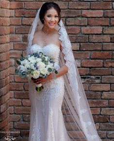 a woman in a wedding dress and veil holding a bouquet with white flowers on it