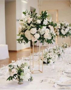 the table is set with white flowers and greenery in vases for centerpieces