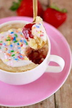 a spoonful of ice cream with sprinkles in a white cup on a pink plate