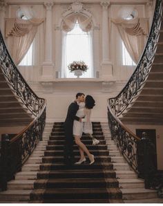 two people are kissing on the stairs in front of a large window and staircases