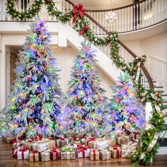 three christmas trees with lights and presents under the banisters in front of them