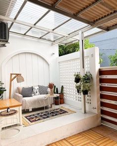 an outdoor living area with white walls and wooden flooring, potted plants on either side of the couch