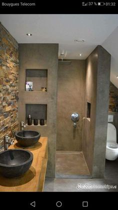 two black bowls are on the counter in this modern bathroom with stone walls and flooring