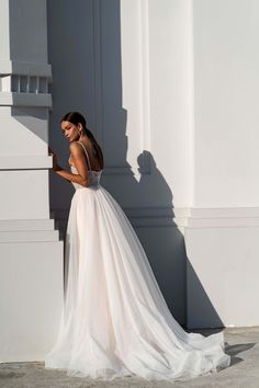 a woman in a white wedding dress leaning against a wall and looking at her phone