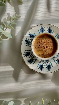 a cup of coffee sitting on top of a saucer next to some green leaves