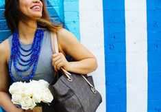 a woman holding a bouquet of flowers and a handbag in front of a blue wall