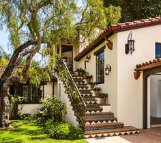 a white house with steps leading up to the front door and entry way, surrounded by greenery