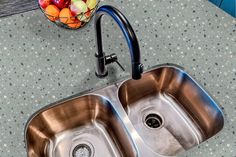 two stainless steel sinks in a kitchen next to a bowl of fruit on the counter