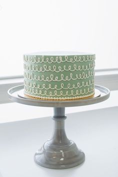 a green and white cake sitting on top of a metal stand next to a window