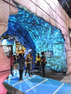 several people are standing in front of a large blue rock formation at an indoor mall