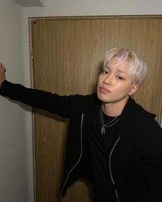 a young man with white hair and black jacket standing in front of a wooden door