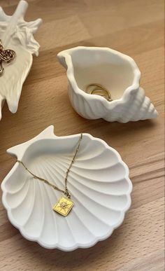 three seashells and two gold necklaces on a wooden table with white dishes