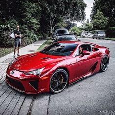 a red sports car parked on the side of a road next to a person walking