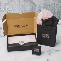 two black boxes with pink tissue paper in them sitting on a marble countertop next to one box that says melanie golden