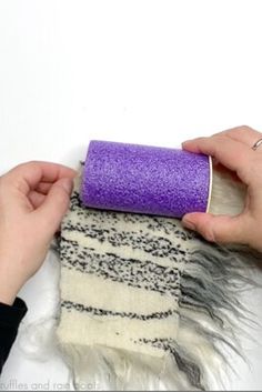 two hands are holding a purple roll of fabric and another hand is placing it on top of a white rug