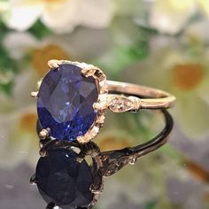 an oval shaped blue sapphire and diamond ring on top of a flowered surface with flowers in the background