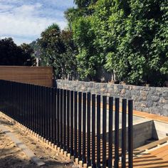 a black iron fence is next to a stone wall and tree lined area in the background