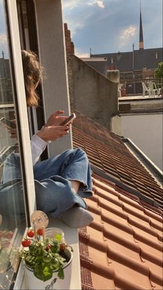 a woman sitting on top of a window sill looking at her cell phone