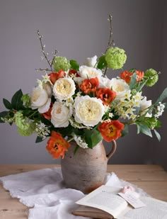 a vase filled with white and orange flowers on top of a table next to an open book