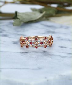 a gold ring with red stones on it sitting on a marble table next to dried leaves