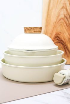 three white dishes stacked on top of each other in front of a wooden board with earbuds