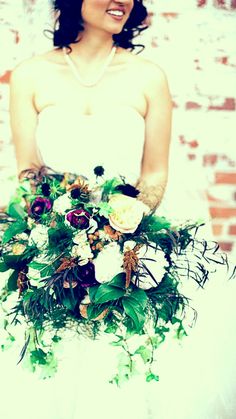 a woman in a wedding dress holding a bridal bouquet with greenery and flowers