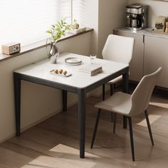 a white table with two chairs and a coffee pot on it in front of a window