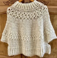 a white crocheted sweater hanging on a wooden hanger